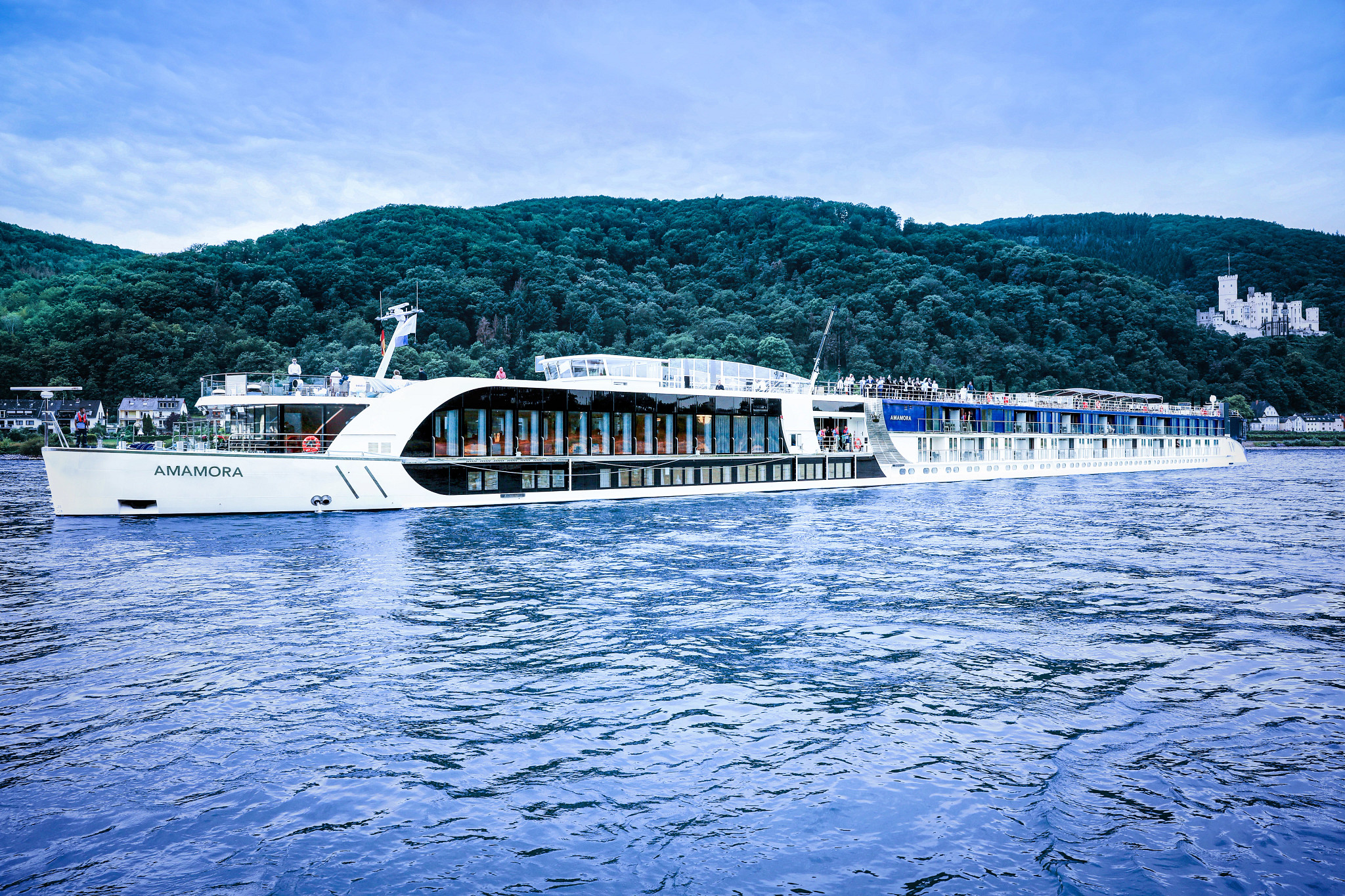 AmaMora river cruise ship sailing on the Rhine with castle and forested hills