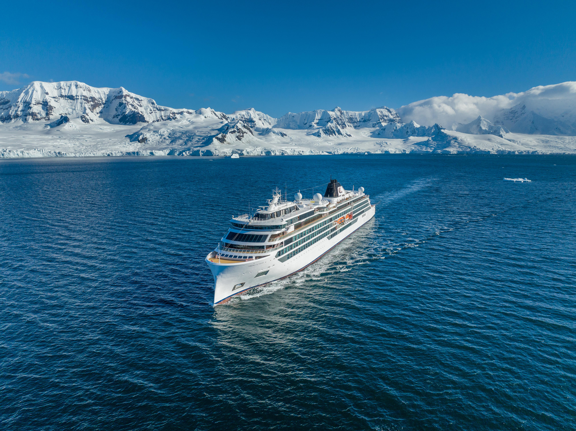 A white luxury cruise ship navigating through deep blue waters with a dramatic snow-covered