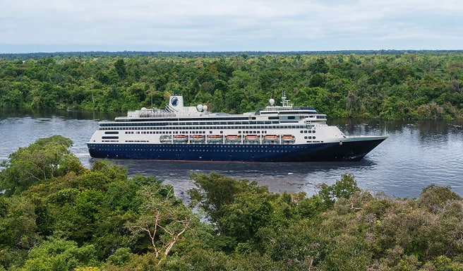 Cruise Ship in Lush Tropical Waterway A dark blue and white cruise ship navigating through a narrow river surrounded by dense, green
