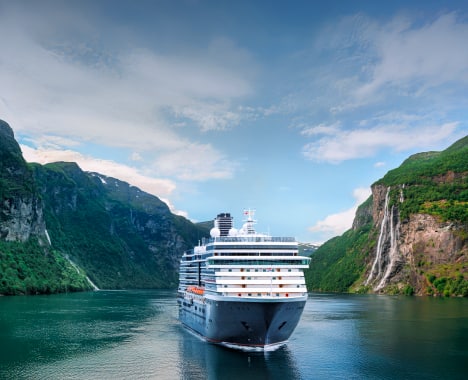 Cruise Ship in Norwegian Fjord Holland America cruise ship navigating through a dramatic Norwegian fjord with steep green mountains and a cascading waterfall