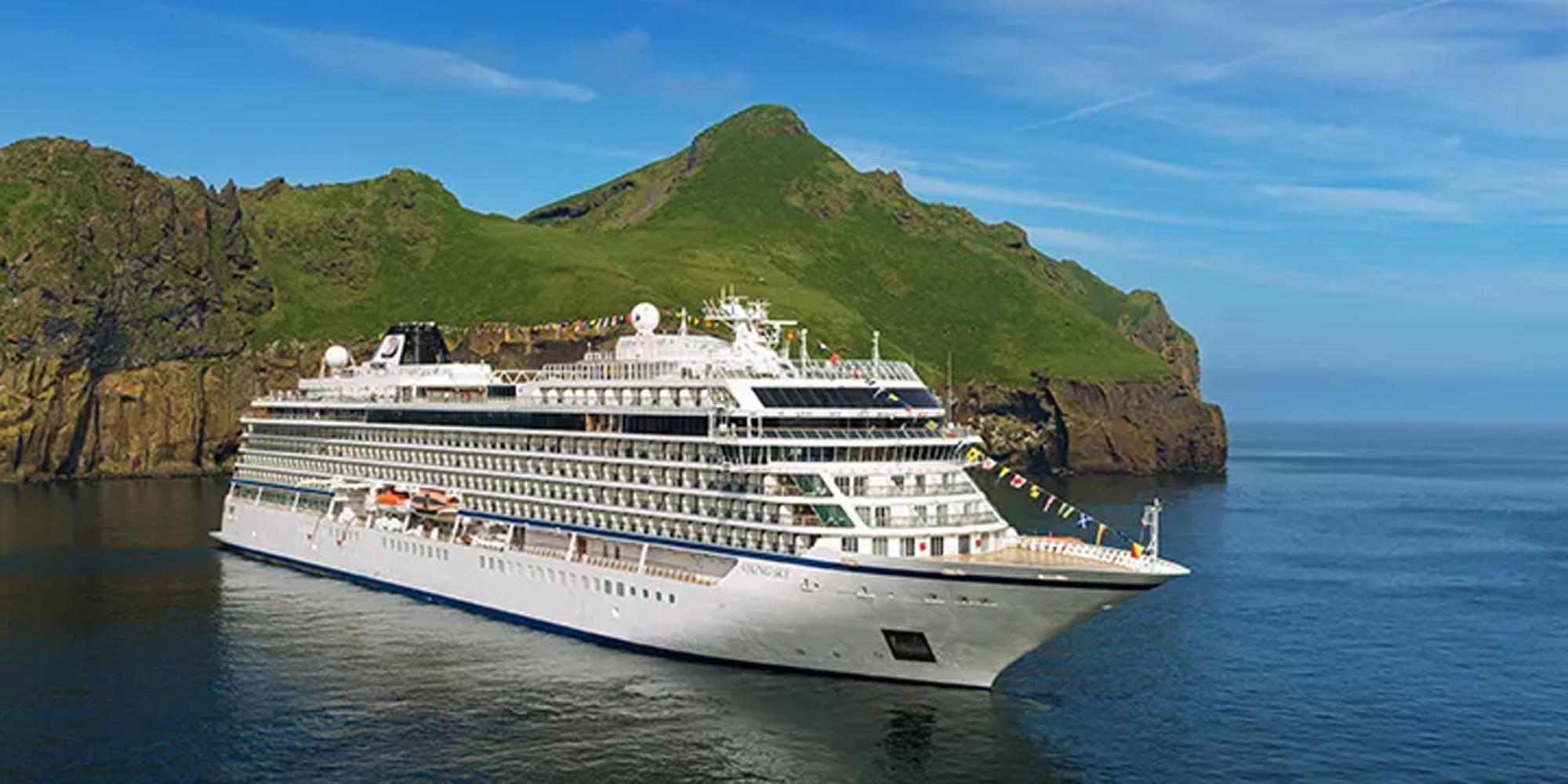 Viking cruise ship sailing near a green mountainous volcanic island