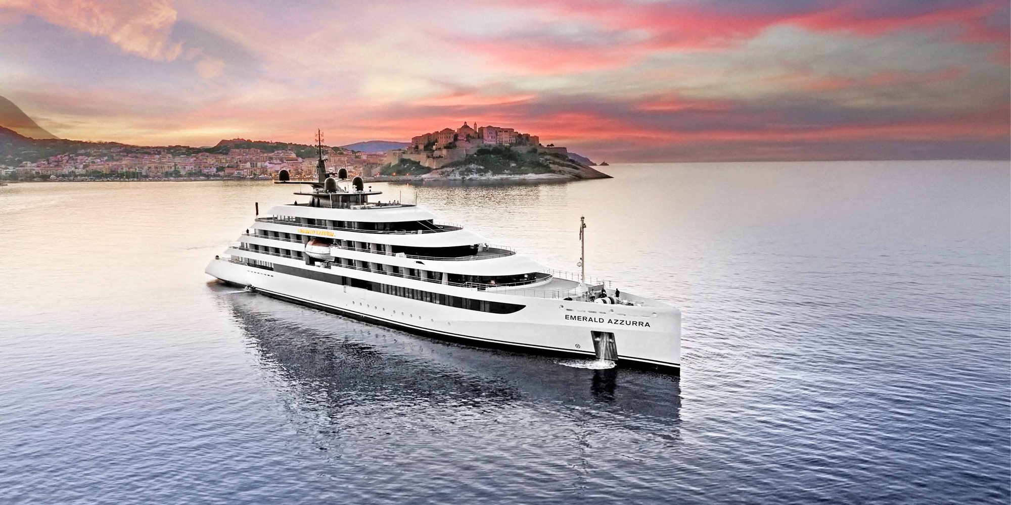 A sleek white luxury yacht named Emerald Azzurra cruising near a picturesque Mediterranean coastal