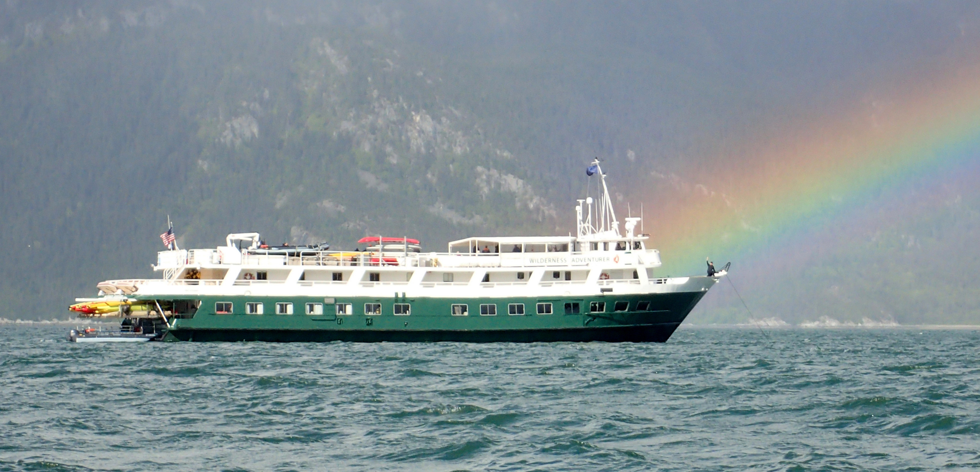 Green Cruise Ship with Rainbow Backdrop A green and white expedition or cruise ship sailing on choppy waters with a vivid rainbow arching