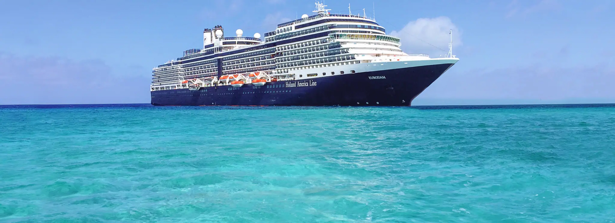 Holland America Cruise Ship at Sea A large blue and white Holland America cruise ship sailing on turquoise Caribbean waters under a clear blue sky.