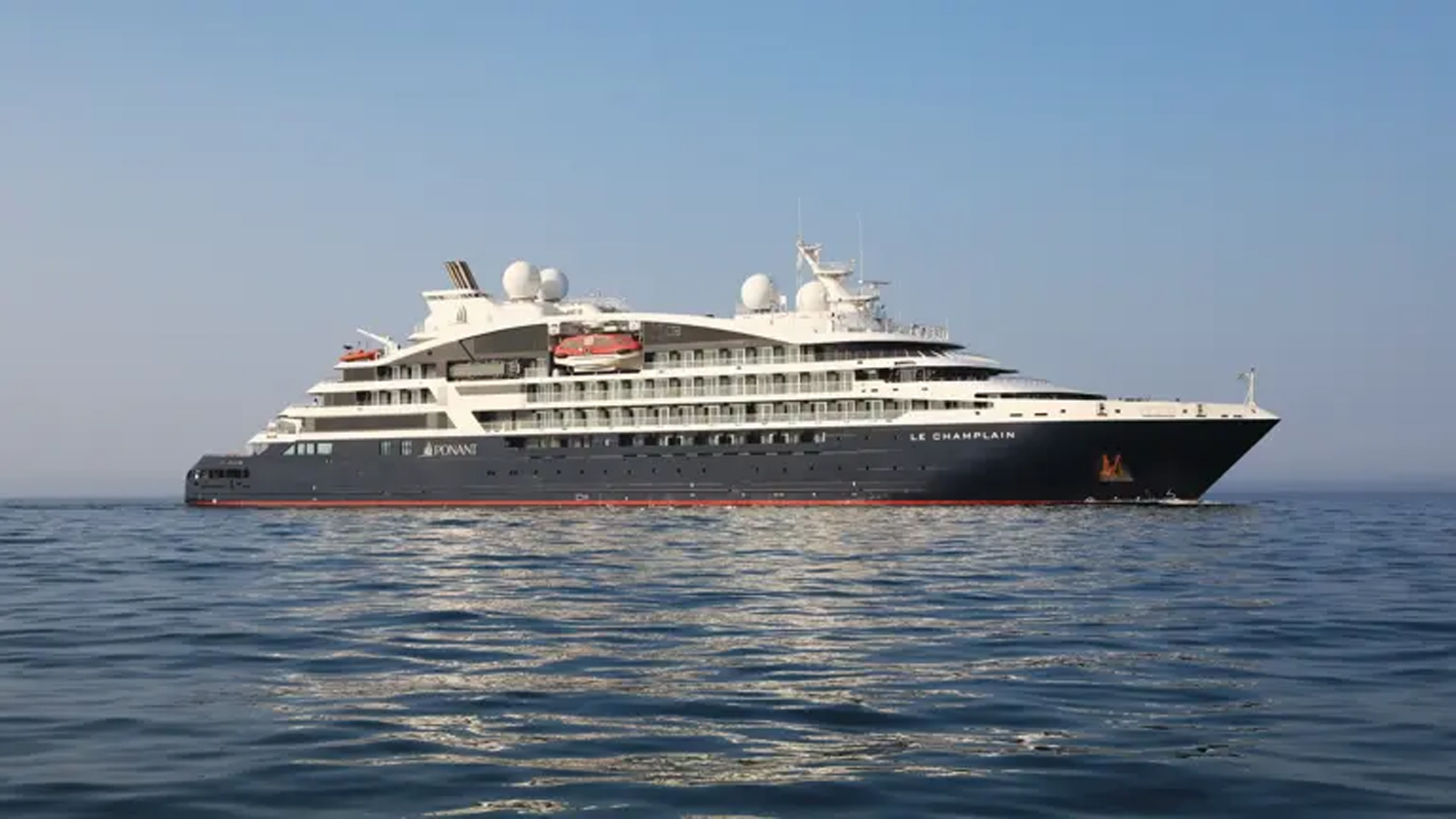 Le Champlain Luxury Expedition Cruise Ship A sleek white and dark gray luxury expedition cruise ship sailing on calm blue waters. The vessel