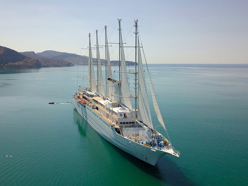 Windstar sailing yacht anchored in tranquil turquoise waters with mountainous coastline