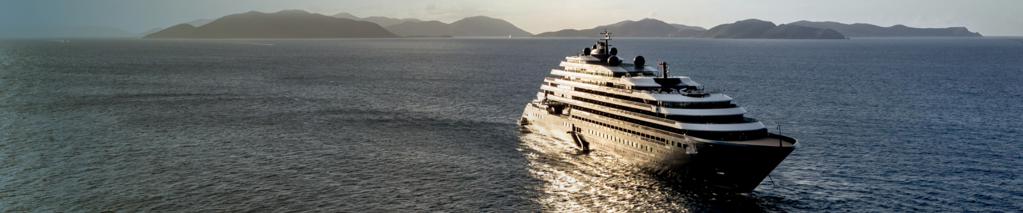 Ritz-Carlton luxury yacht sailing along a scenic mountain coastline