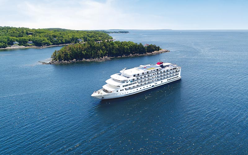 Luxury Cruise Ship in Coastal Landscape A white cruise ship sailing near a forested coastline with rocky shores and green islands