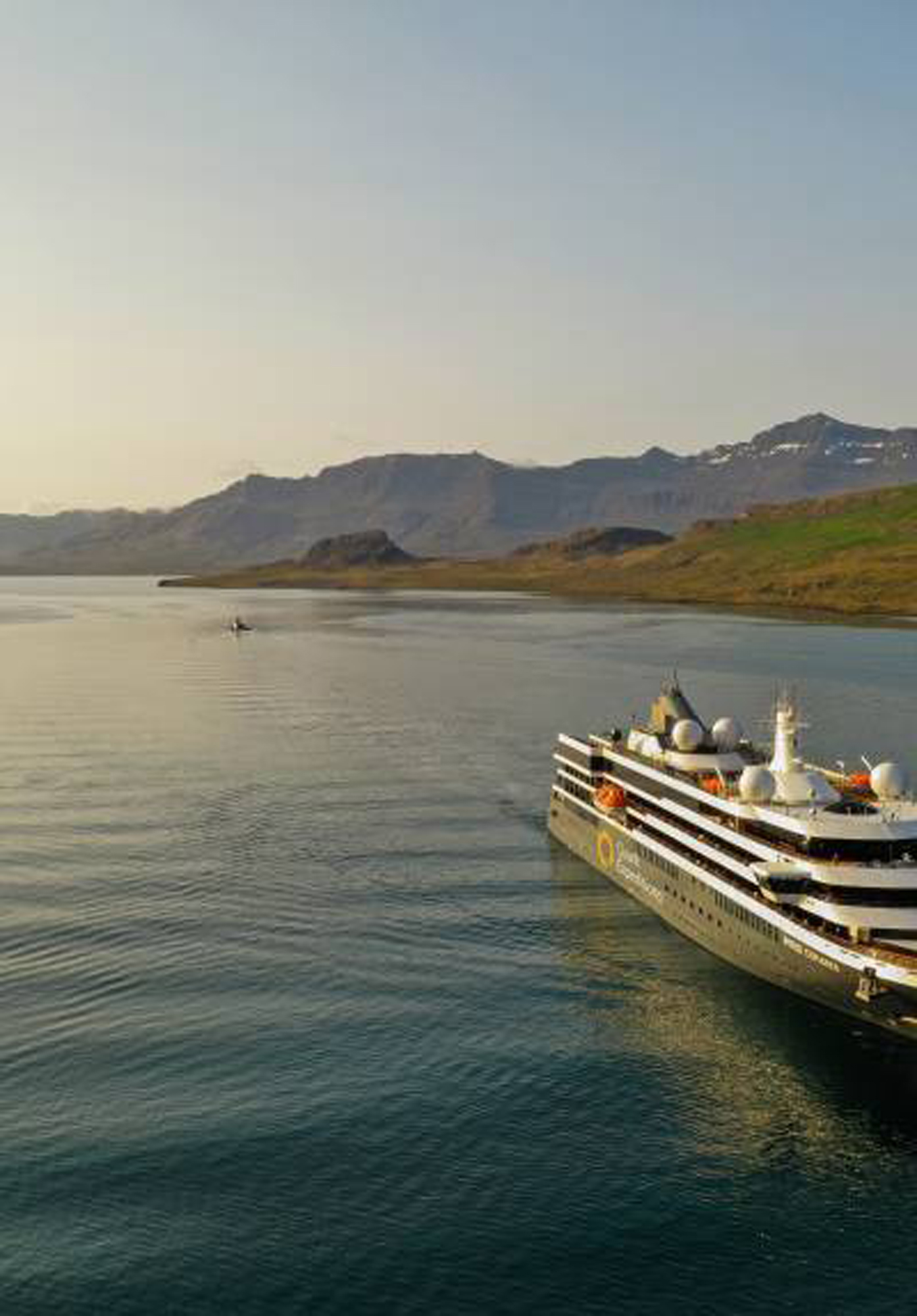 Ritz-Carlton luxury cruise ship sailing through calm waters with mountain scenery