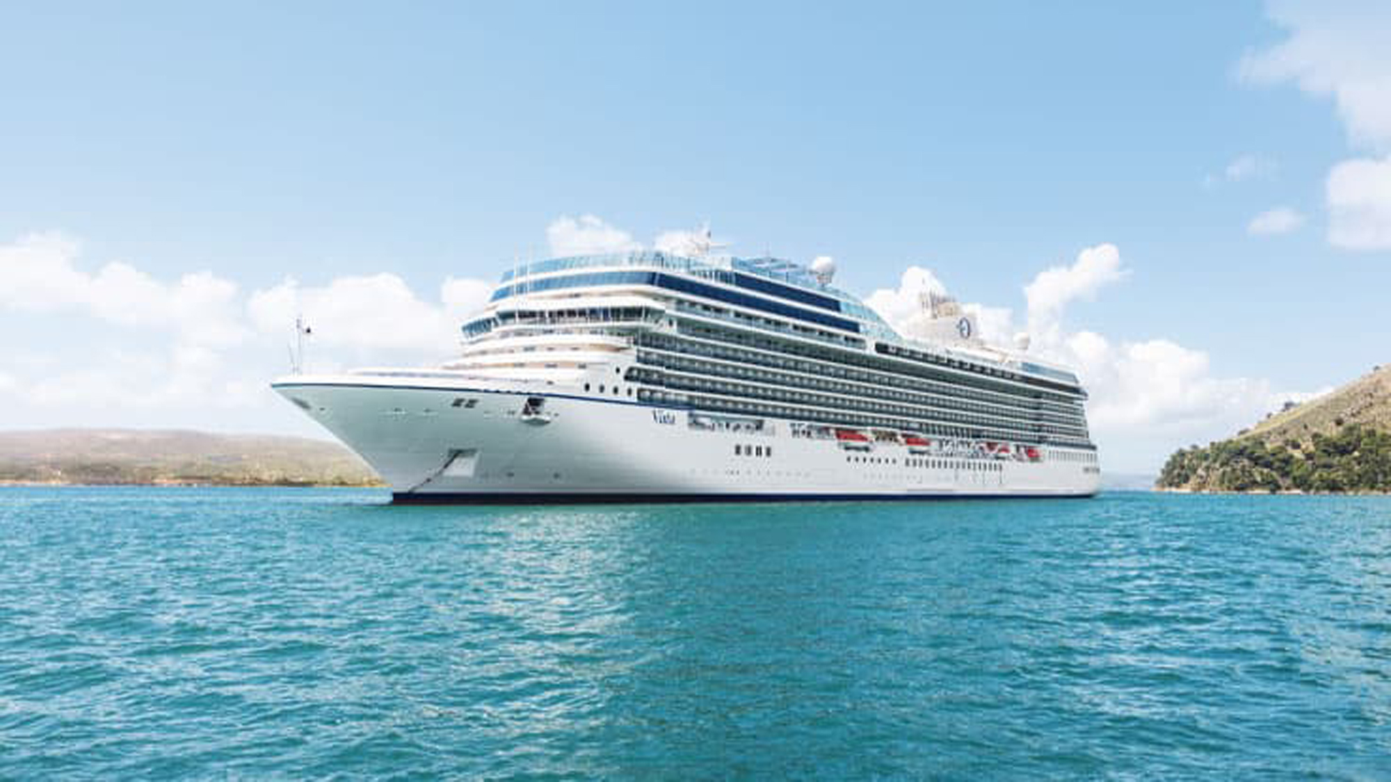 A pristine white and blue cruise ship anchored in crystal-clear turquoise waters near a rocky