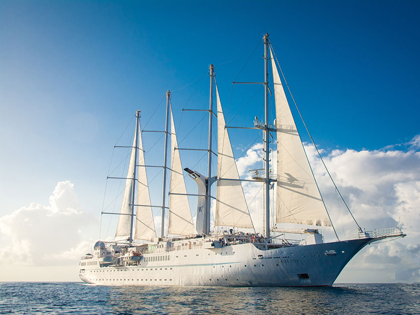 Windstar sailing yacht with white sails fully extended cruising on bright blue waters