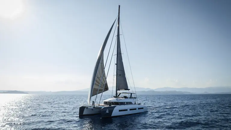 Modern Catamaran Sailing on Blue Waters A sleek white and gray catamaran sailing with fully raised sails on a calm, blue ocean with distant