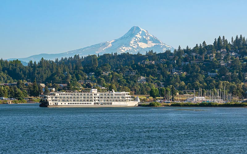 Mount Hood River Cruise Scenic View A river cruise ship docked near a forested hillside with snow-capped Mount Hood in the background