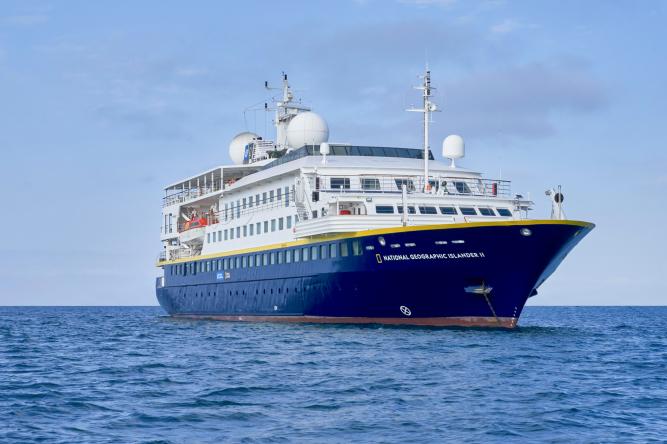 National Geographic expedition cruise ship with blue hull sailing on calm waters
