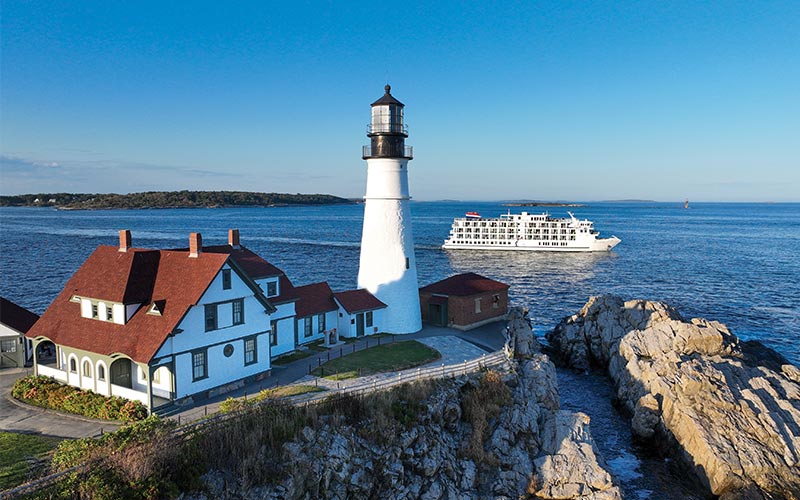 Portland Head Lighthouse with Cruise Ship A white lighthouse with a red-roofed keeper's house sits on rocky coastal terrain, with a white
