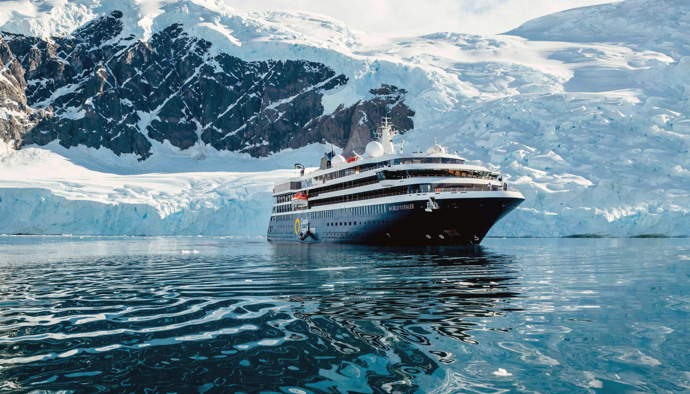 QE_WVO_Exterior-Shots_1 Quark Expeditions ship navigating through icy waters with snow-covered terrain and helicopter overhead
