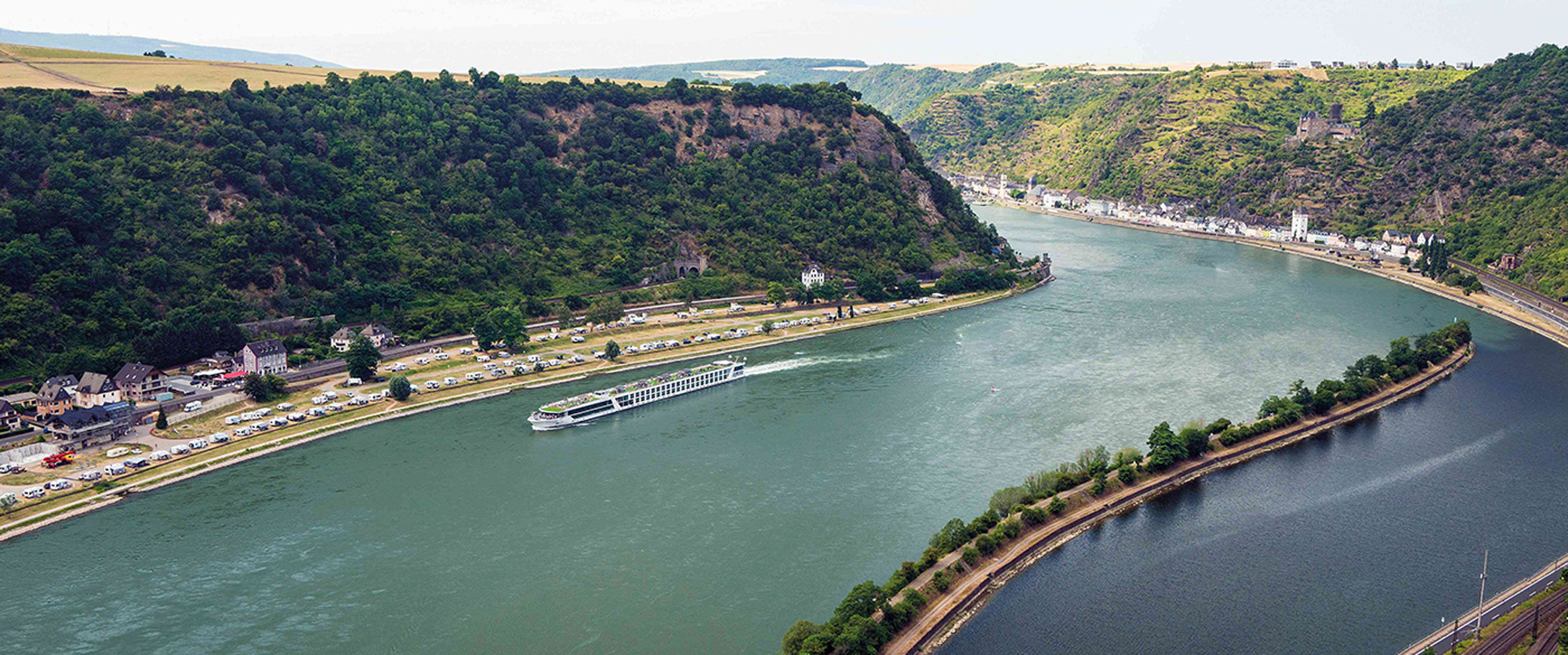 Rhine River cruise through scenic valley with forested cliffs and charming riverside village