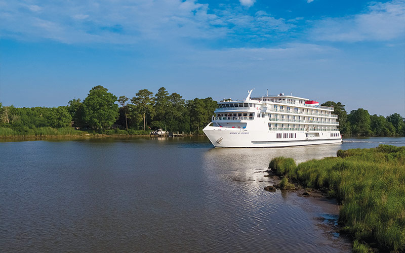 River Cruise Ship on Scenic Waterway A white river cruise vessel sailing through a serene waterway with lush green trees and grassy shorelines