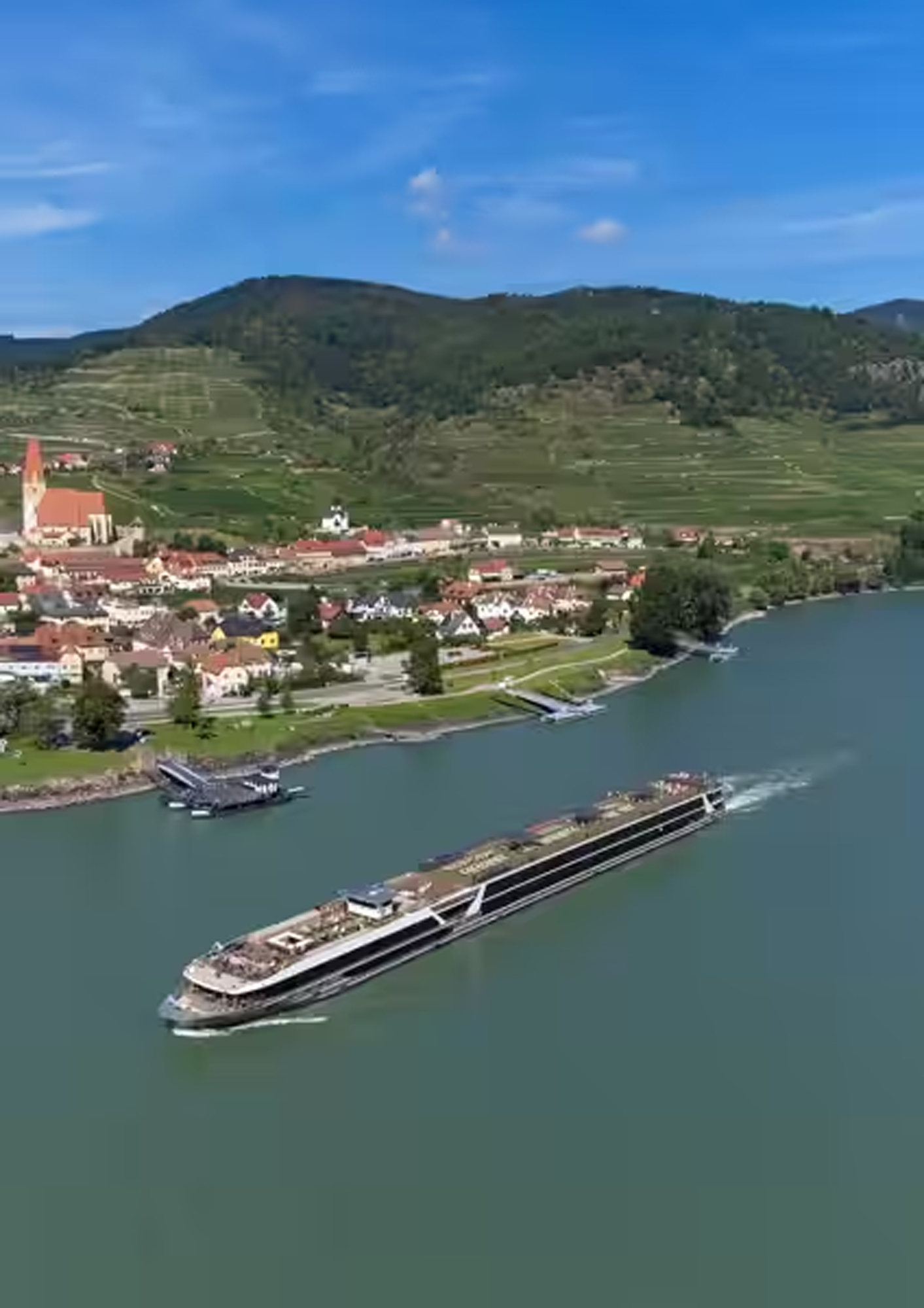 River Cruise Through European Vineyard Landscape A modern river cruise ship sailing along a picturesque waterway with a charming European village