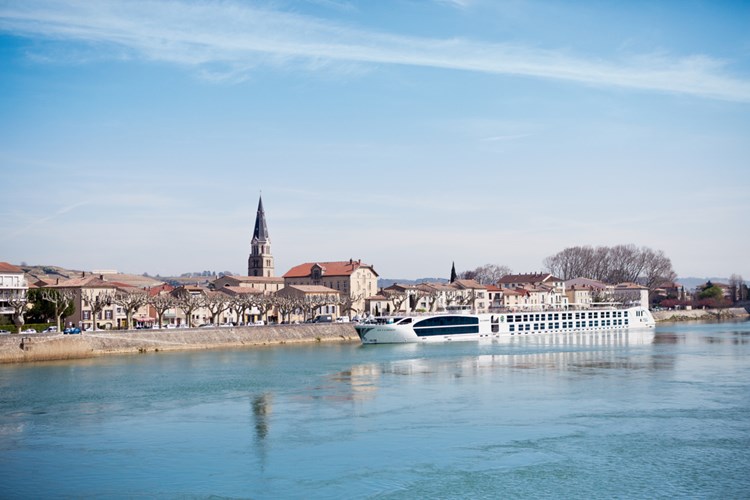 A white river cruise ship docked alongside a picturesque European town with a prominent church