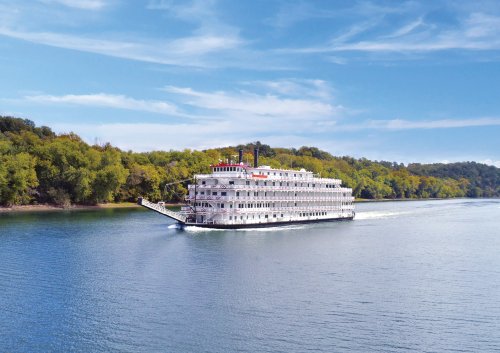 Riverboat Cruising Scenic Waterway A classic white multi-deck riverboat navigates a serene river surrounded by lush green forested