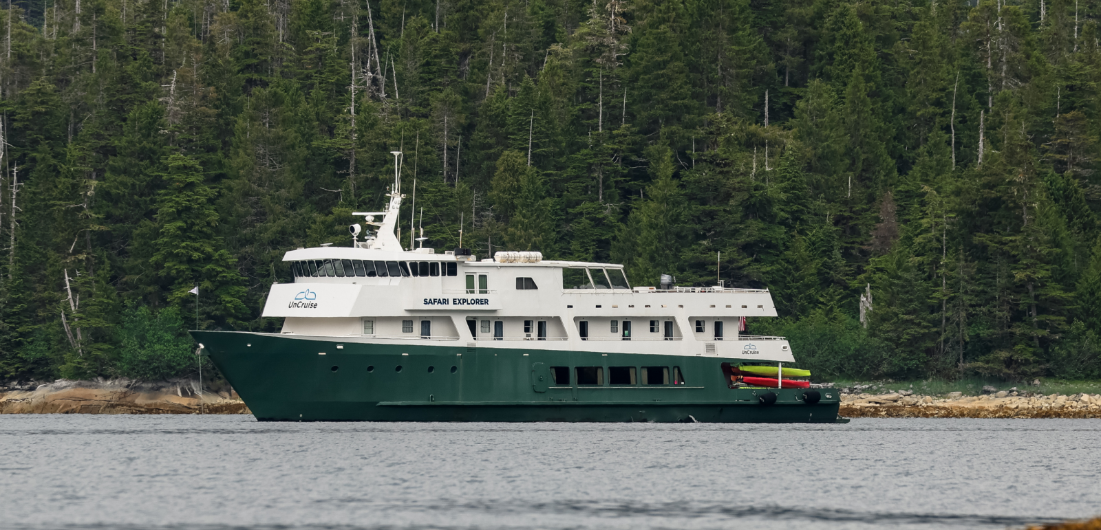 Safari Explorer Vessel in Coastal Forest A green-hulled expedition cruise ship named Safari Explorer anchored near a rocky shoreline