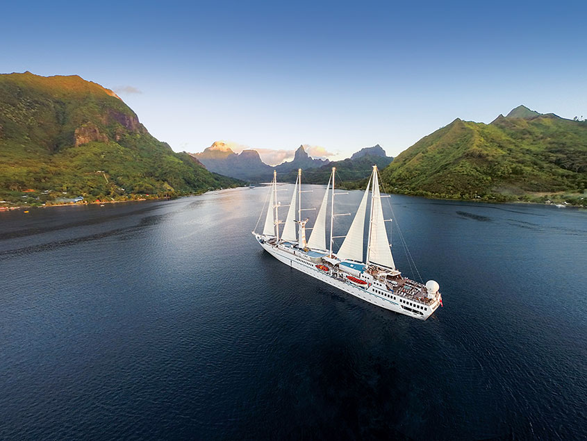 Windstar sailing vessel navigating through scenic waterway with lush green mountains