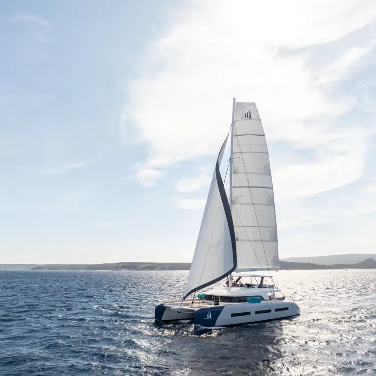 Sleek White Catamaran Sailing Blue Waters A modern white catamaran with fully raised sails navigating through bright blue ocean waters