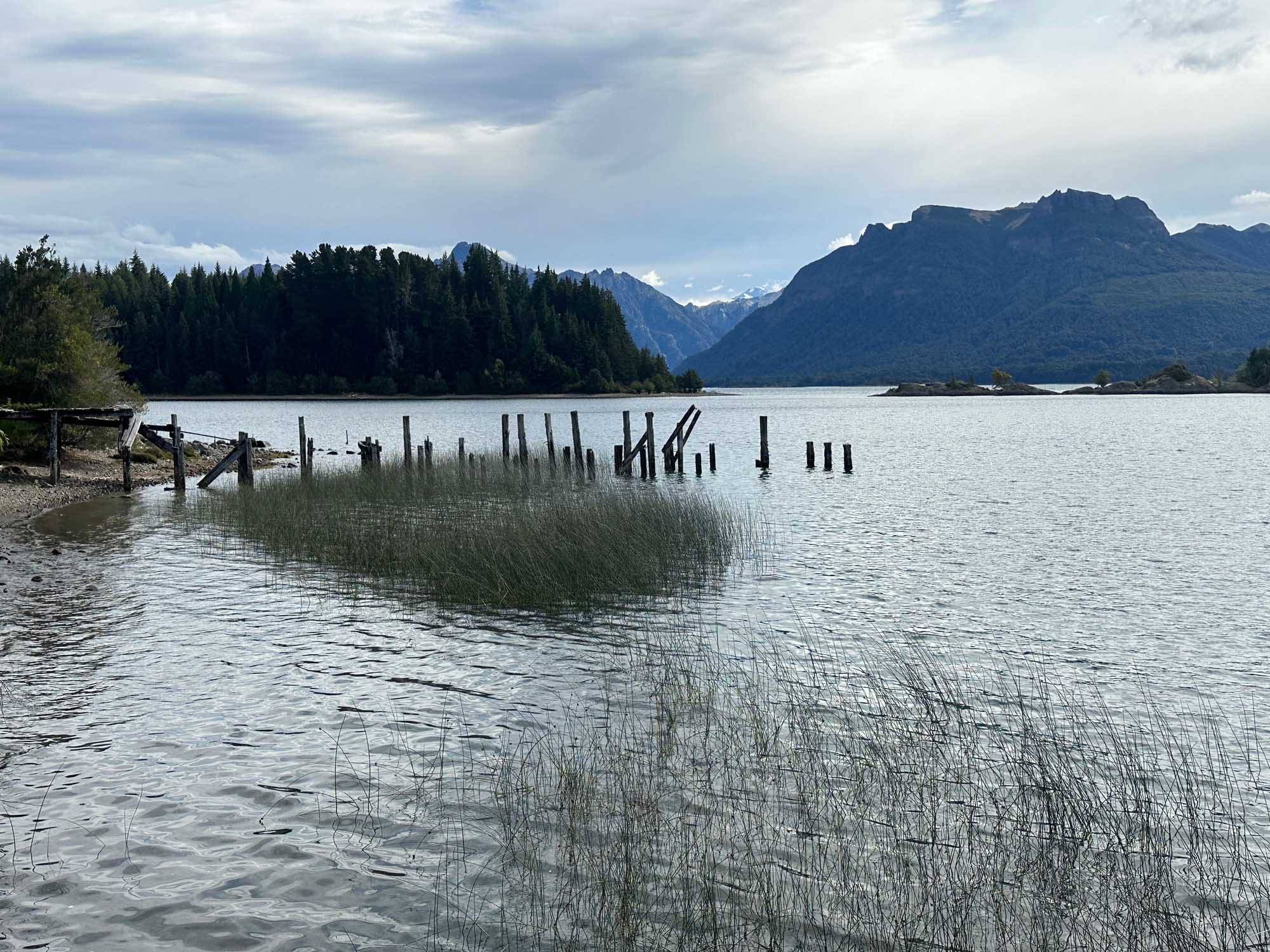 Alpine Lake with Mountain Backdrop and Historic Pier A serene alpine lake scene featuring weathered wooden pilings and native marsh grasses in