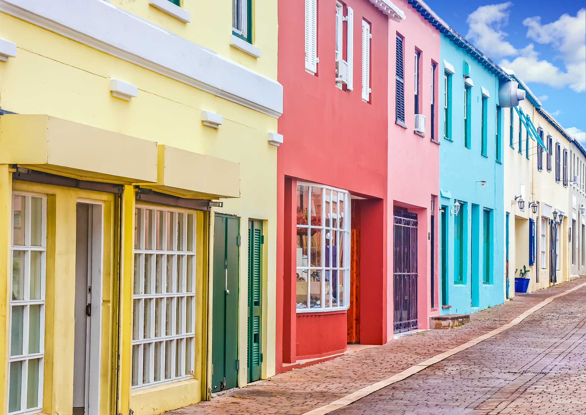 Colorful Colonial Architecture in Bermuda A picturesque street lined with vibrant pastel-colored colonial buildings featuring yellow, pink, turquoise, and cream facades.