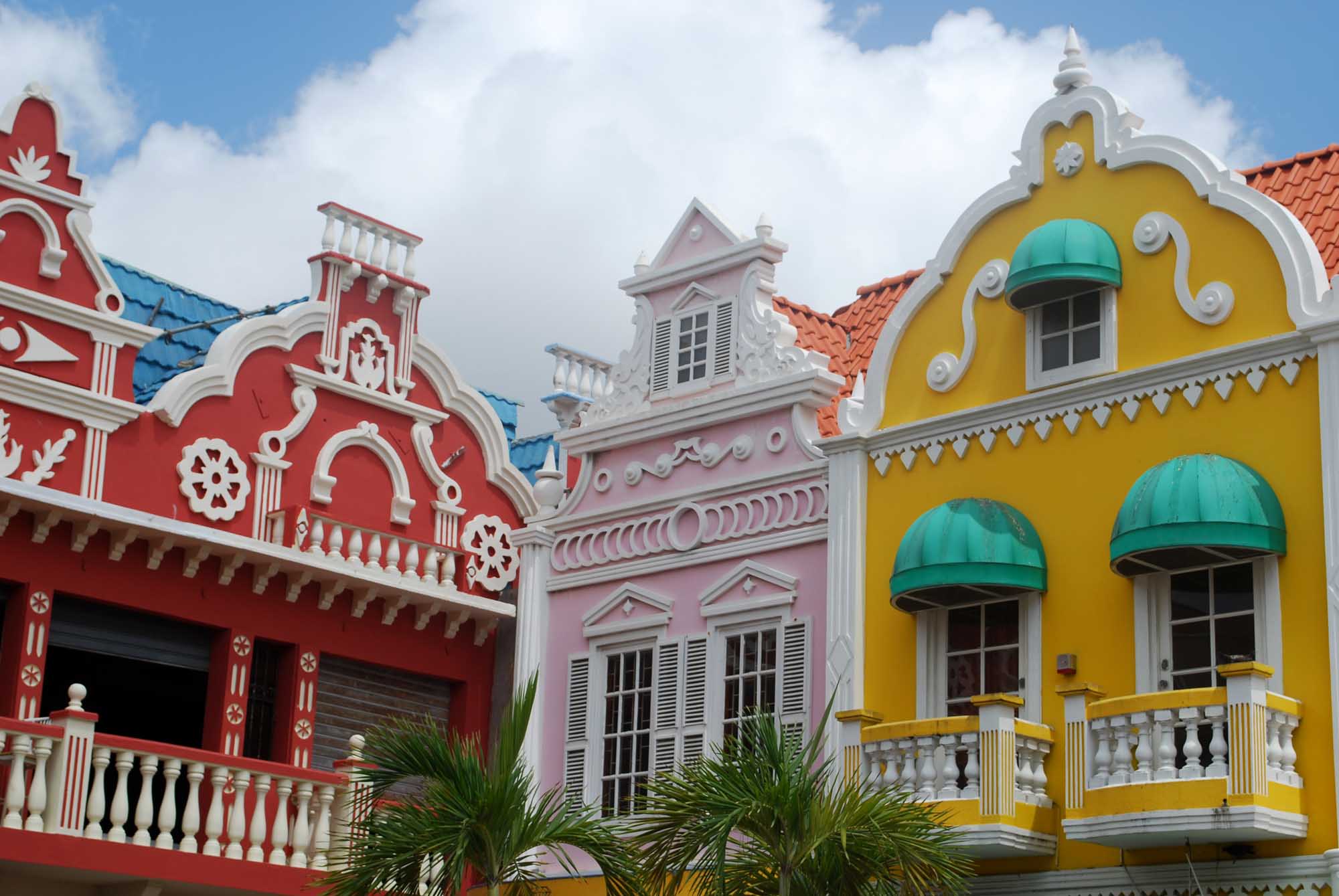 Colorful Colonial Architecture in Willemstad A vibrant row of Dutch Colonial buildings featuring bold primary colors—red, pink, and yellow—with white ornamental trim, arched windows, and turquoise awnings. The iconic architecture reflects Caribbean colonial heritage with distinctive peaked roofs and decorative balustrades, typical of Curaçao's historic waterfront district.