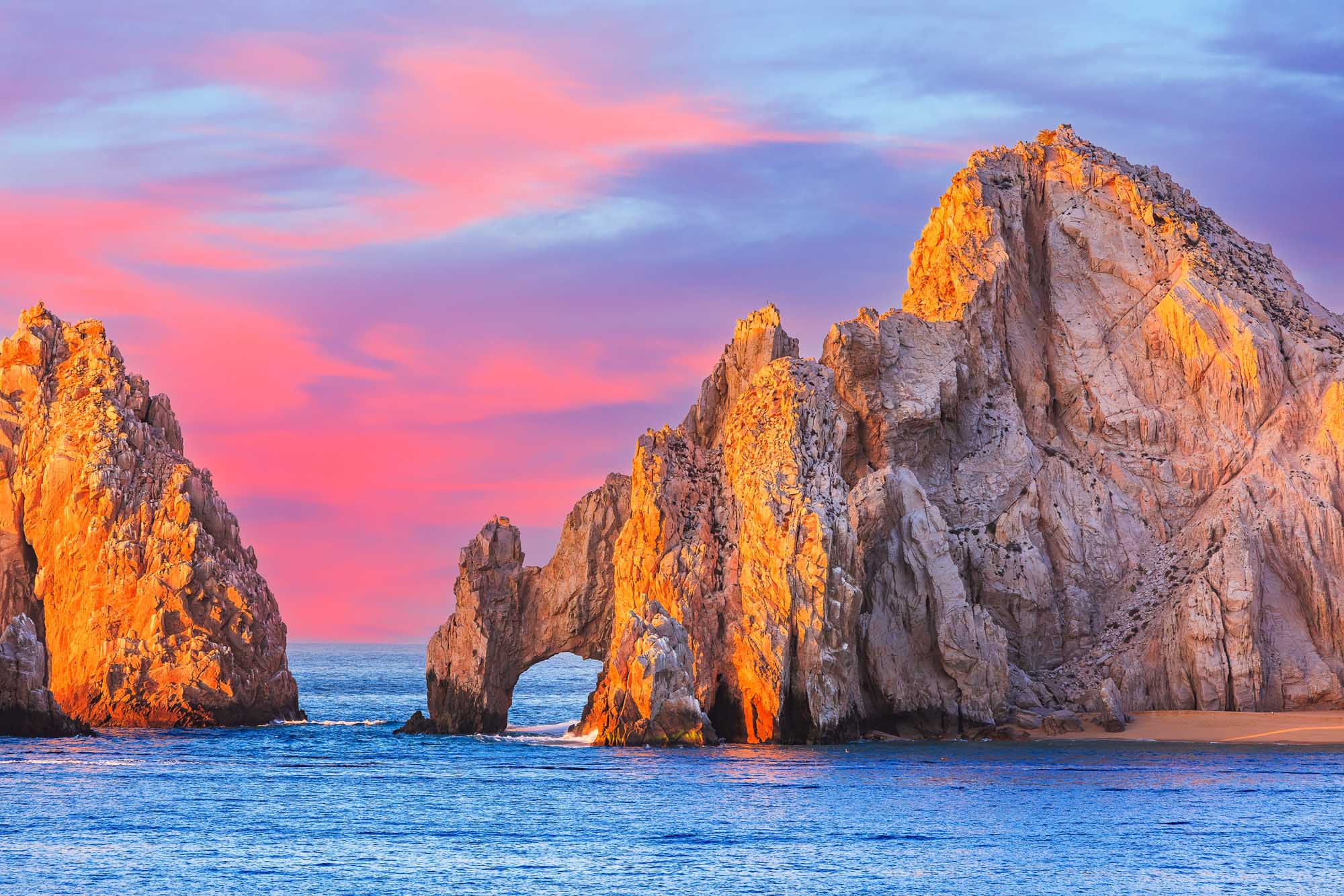 El Arco Rock Formation at Sunset, Cabo San Lucas The iconic El Arco (The Arch) rock formation at Cabo San Lucas is bathed in golden sunset light, with dramatic granite cliffs rising from the turquoise Pacific waters. The striking natural landmark features a natural arch carved through the rock, creating a spectacular gateway between the land and sea, with vibrant pink and purple hues filling the sky.