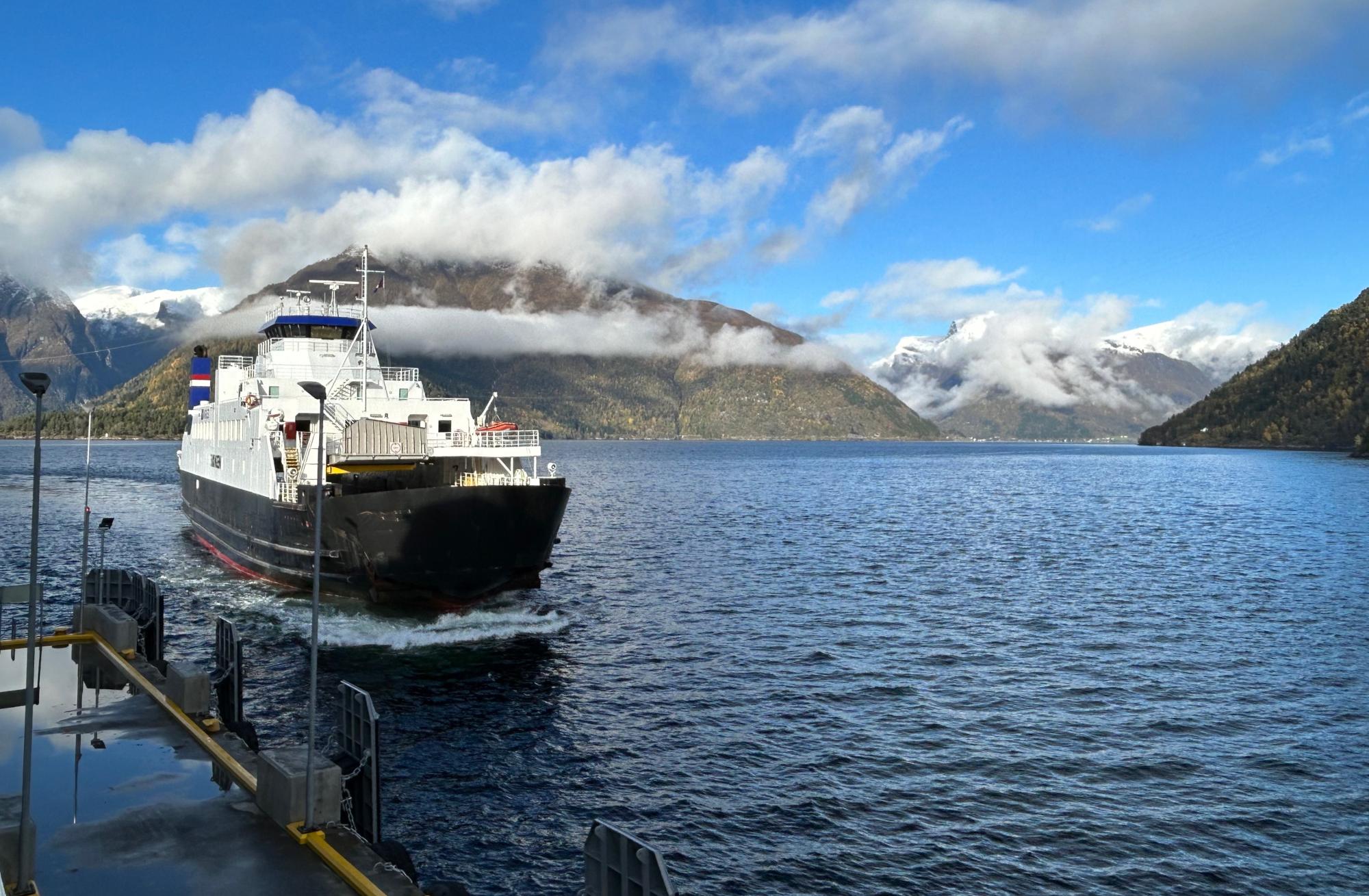 Ferry Departing Patagonian Lake with Snow-Capped Mountains A white and black passenger ferry with Dutch flag markings departs from a dock on a pristine alpine
