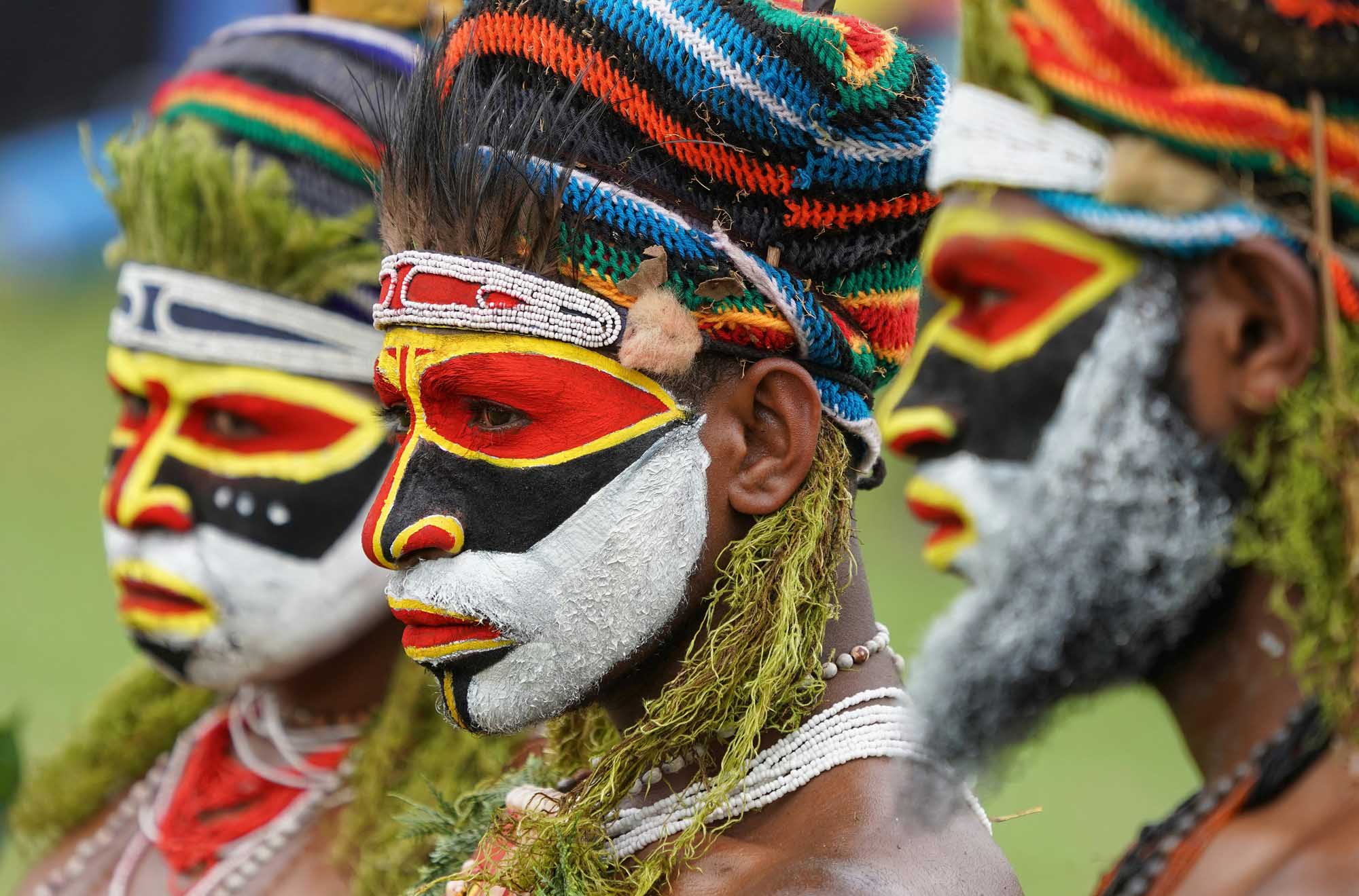 Members of an indigenous tribe from Papua New Guinea display elaborate traditional face paint in bold red, yellow, black, and white geometric patterns, complemented by colorful woven headdresses and natural fiber decorations. This cultural portrait showcases the rich tribal heritage and ceremonial artistry of the region.