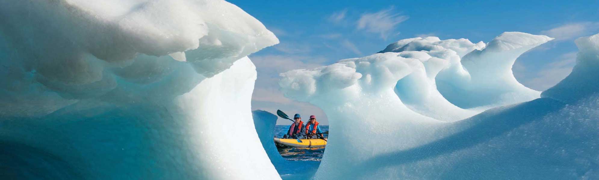 Kayaking Through Arctic Icebergs Two adventurers in a yellow kayak navigate through towering turquoise and white icebergs in Arctic waters under clear blue skies, showcasing the dramatic scale and beauty of polar ice formations.