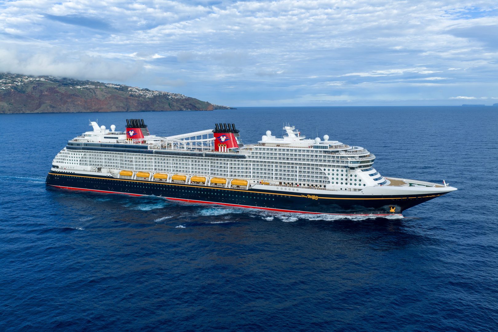 Disney cruise ship anchored off a volcanic island with terraced settlements