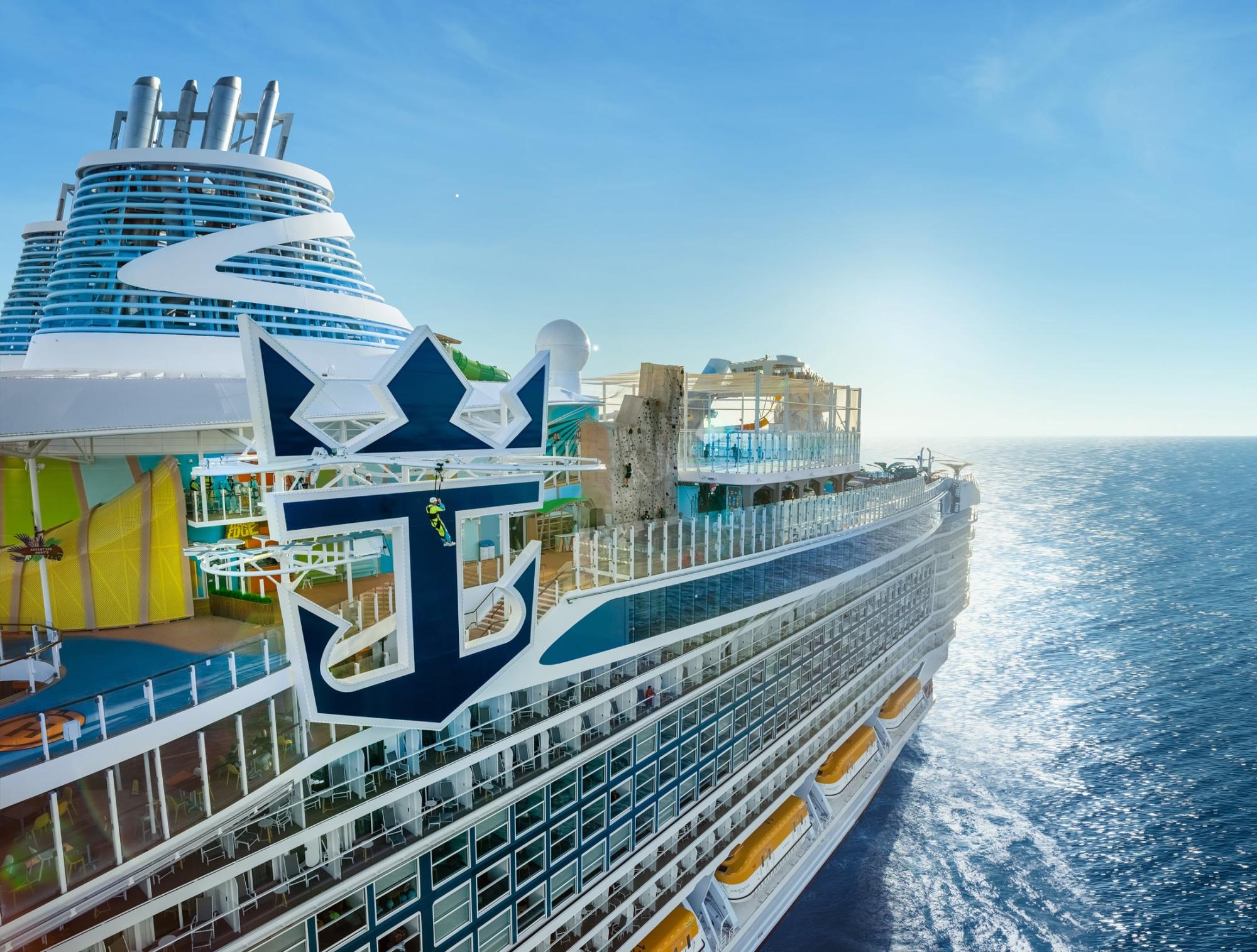 A modern cruise ship with distinctive blue and white livery featuring a large anchor emblem on its hull, photographed from the side while at sea.