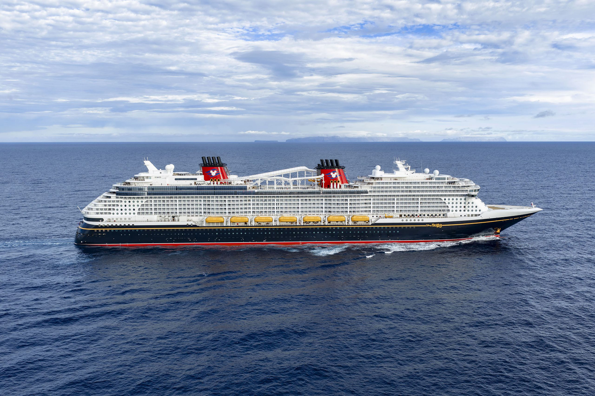 Disney cruise ship sailing through calm blue waters with mountains on the horizon