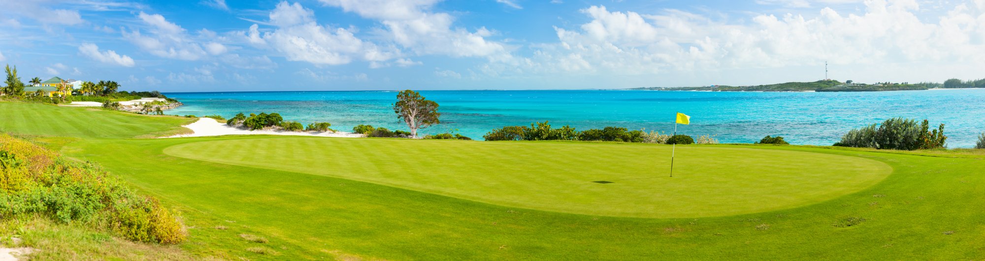 Oceanfront Golf Course with Turquoise Waters A scenic coastal golf course featuring a pristine green fairway overlooking crystal-clear turquoise waters and a white sand beach, with lush tropical vegetation.