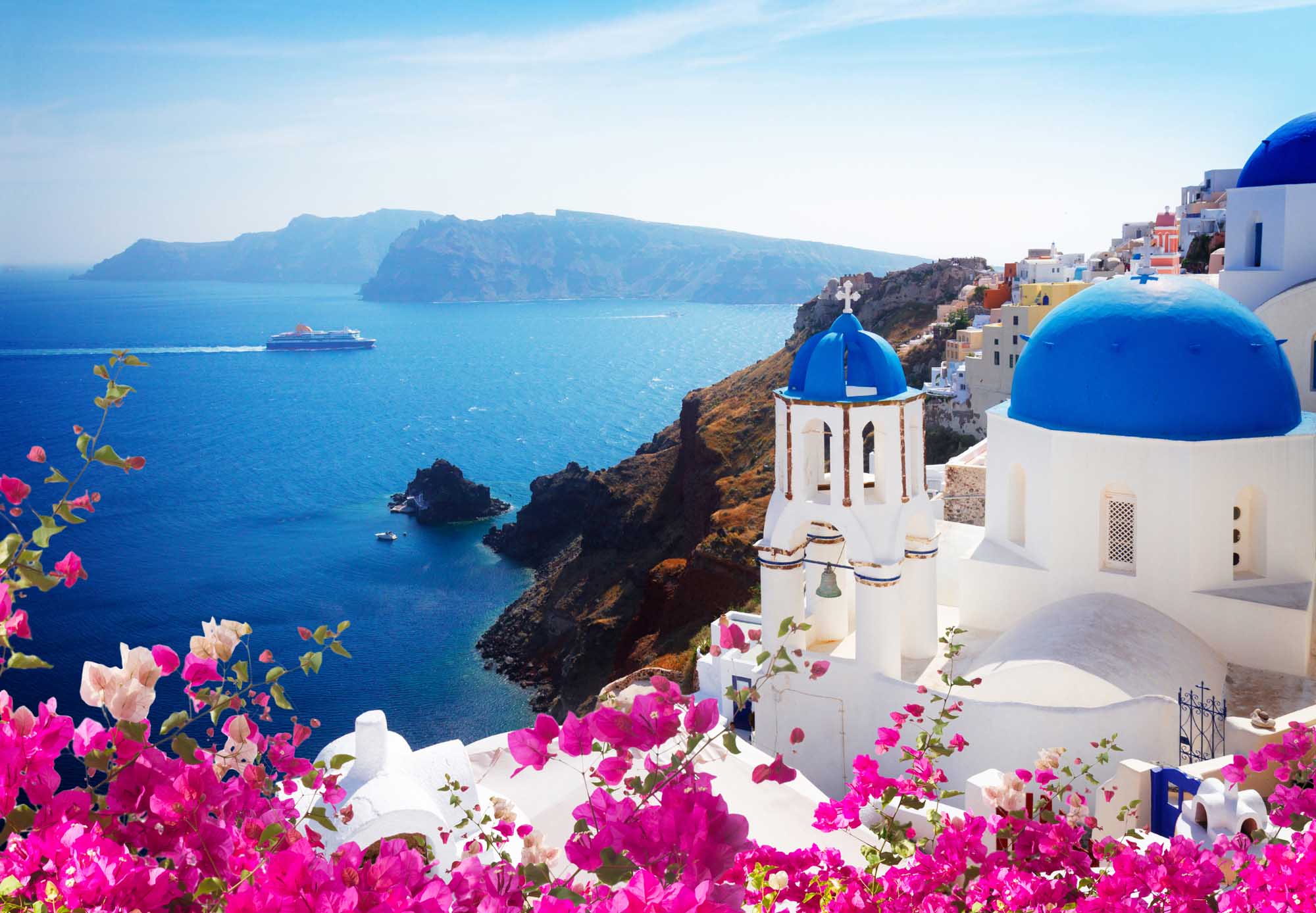 A picturesque view of Oia village in Santorini, Greece, featuring iconic white-washed buildings with brilliant blue-domed churches overlooking the deep blue Aegean Sea.