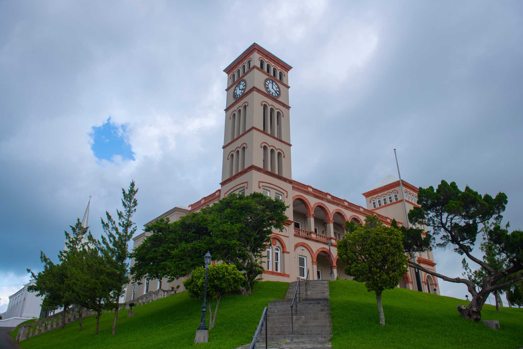 Sessions House Clock Tower in Hamilton, Bermuda A distinctive pink and cream-colored colonial government building featuring a prominent clock tower, situated on a manicured green hillside in Hamilton's city center.