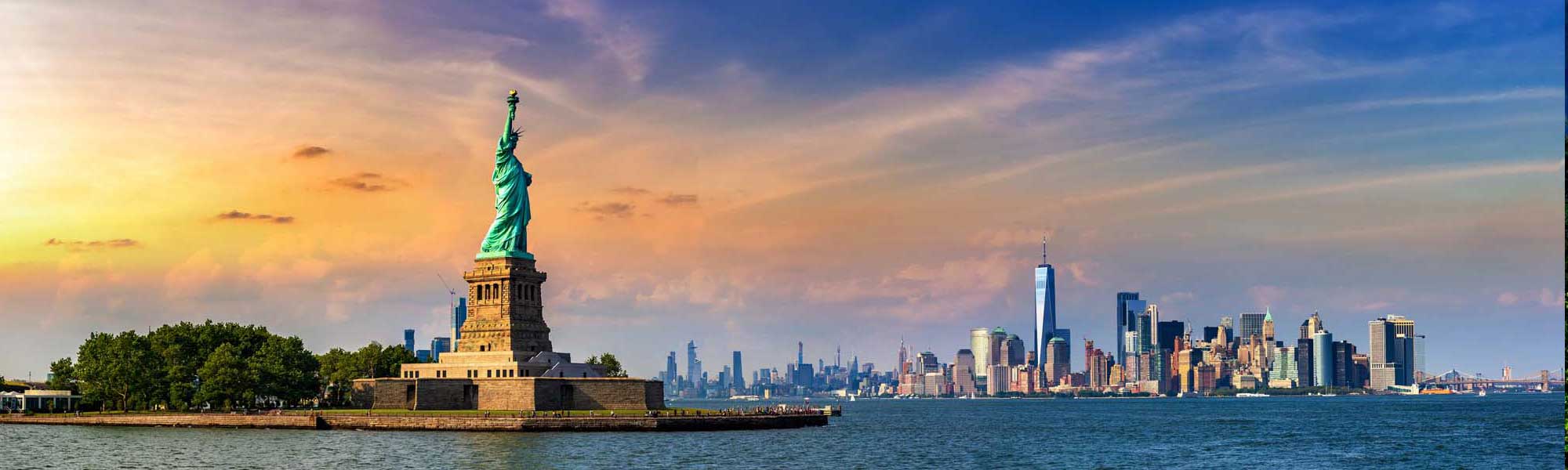 An iconic view of the Statue of Liberty on Liberty Island with the Manhattan skyline illuminated