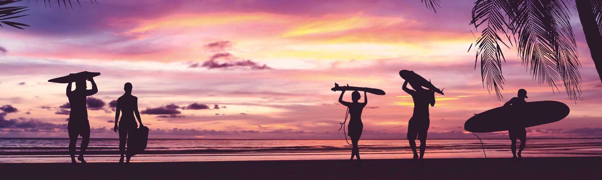 Surfers at Sunset Beach A striking silhouette composition of multiple surfers with their boards gathered on a tropical beach at golden hour, with vibrant pink and purple sunset skies reflected across calm waters and palm fronds framing the scene.
