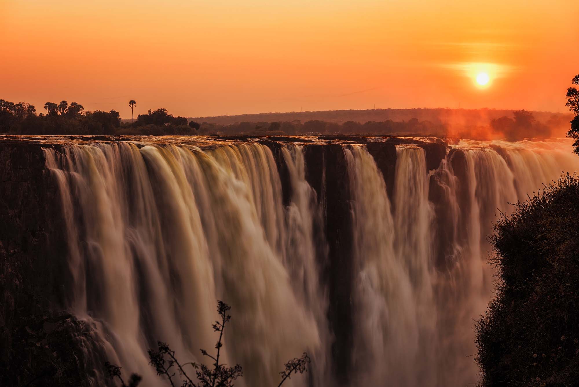 Victoria Falls at Sunset in Golden Light A breathtaking view of Victoria Falls at sunrise or sunset, with massive cascading waterfalls