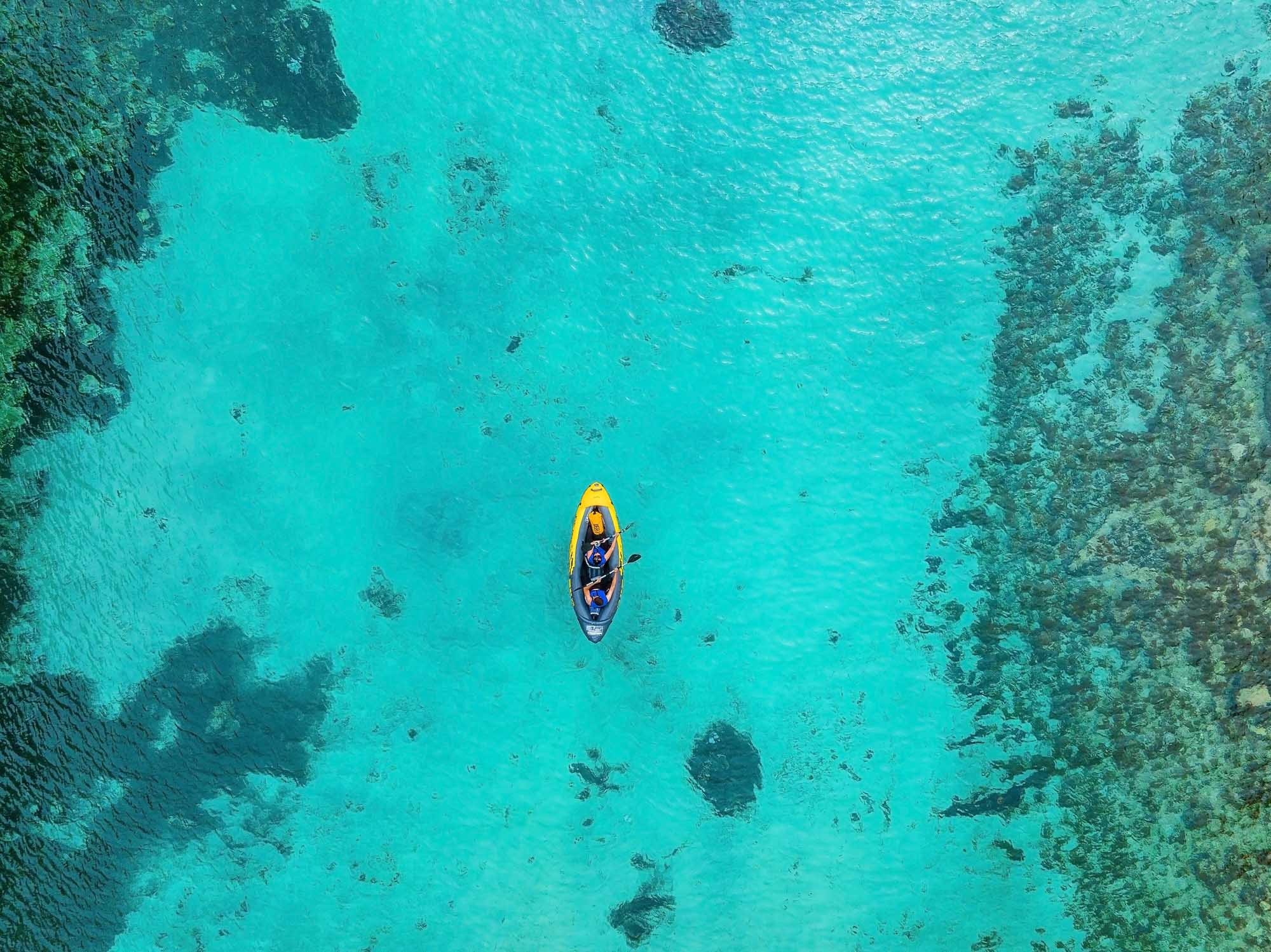 Galápagos Sea Lion on San Cristóbal Beach An aerial view of a lone yellow kayak with a paddler navigating crystal-clear turquoise waters surrounded by rocky outcrops and coral formations.