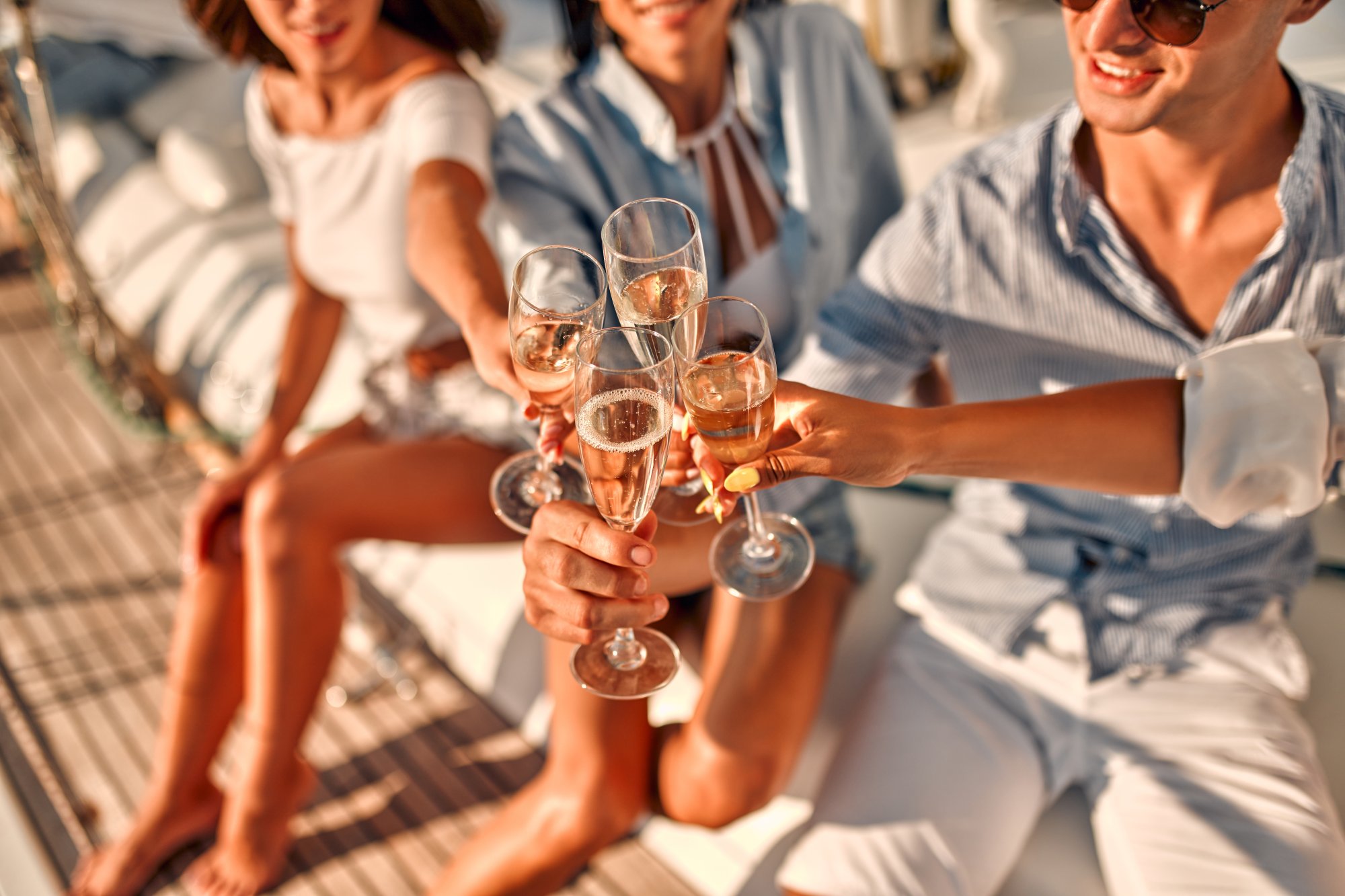 A group of elegantly dressed passengers aboard a cruise ship clink champagne glasses together in a celebratory toast during golden hour.