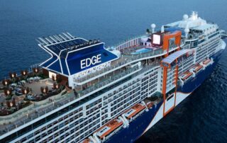 Celebrity Edge cruise ship with blue hull and orange accents in ocean waters
