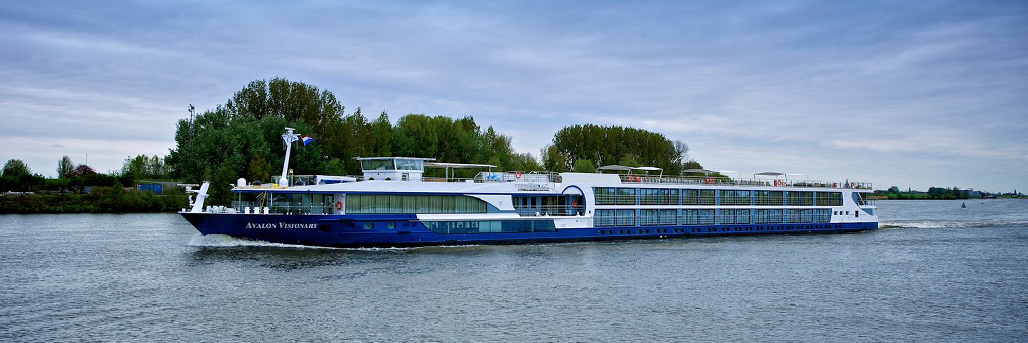 The Avalon Visionary, a modern river cruise ship, sails through a scenic waterway lined with lush