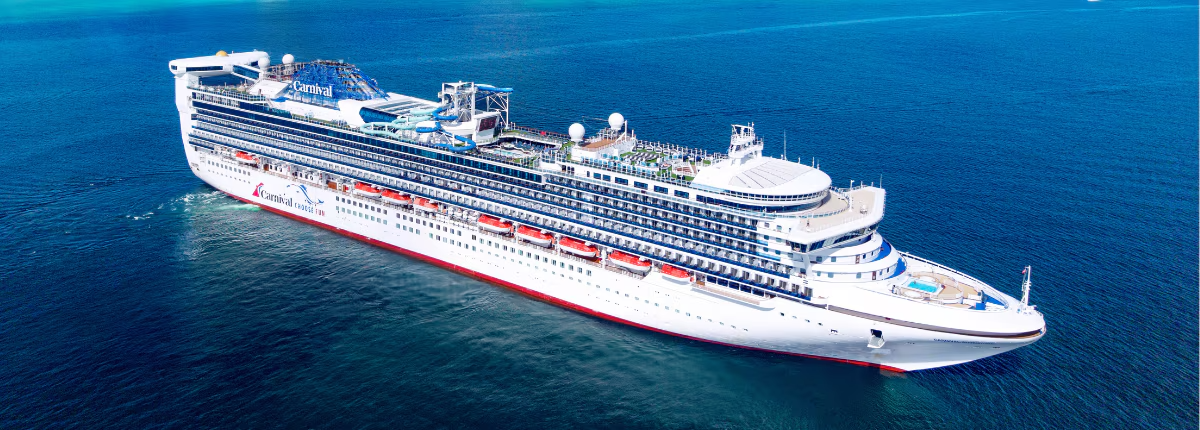 A large modern cruise ship operated by Carnival Cruise Lines sails through deep blue ocean waters