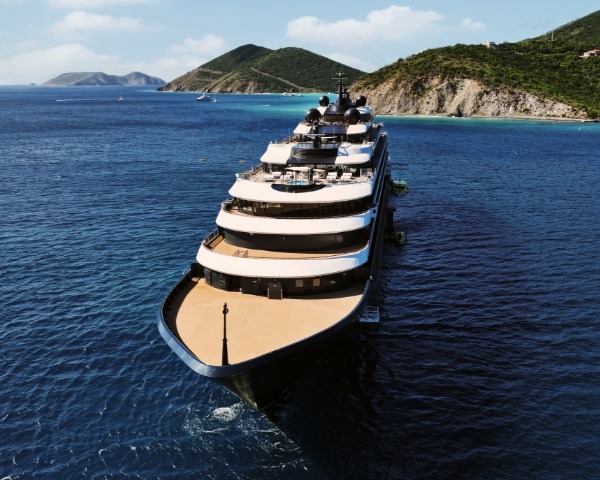 An aerial photograph of a large luxury expedition yacht anchored in crystal-clear Mediterranean